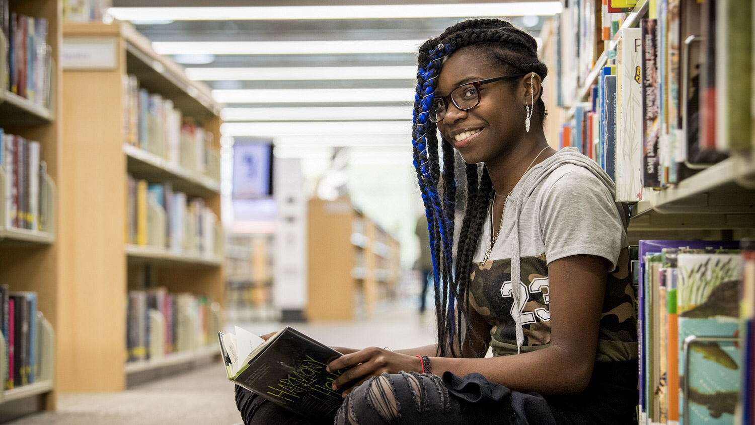 teen library volunteer sitting and smiling among the bookshelves