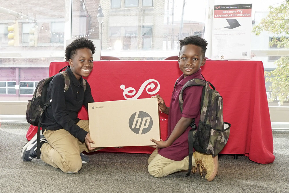 Chromebook distribution at the library - smiling kids with their boxed Chromebook by a Pratt Library table