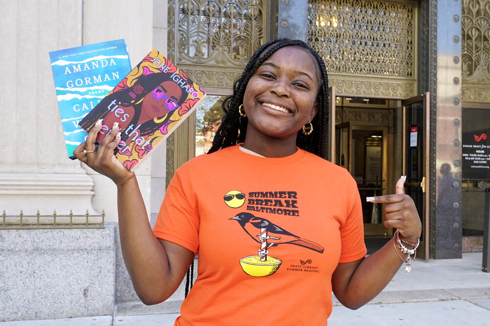 a smiling teen outside the Central Library wearing the 2023 T-shirt, holding 2 free books