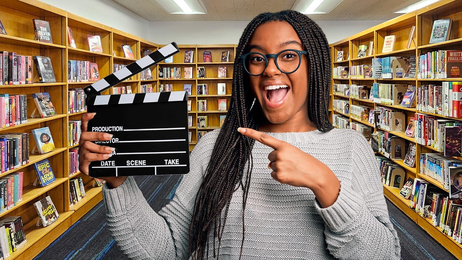 book trailer contest - excited person pointing to a filming clapboard with a background of Pratt Library books for teens