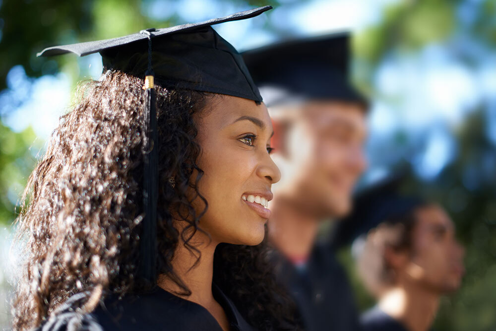 adult graduate with mortarboard cap and gown, and graduates in the background - adult high school diploma