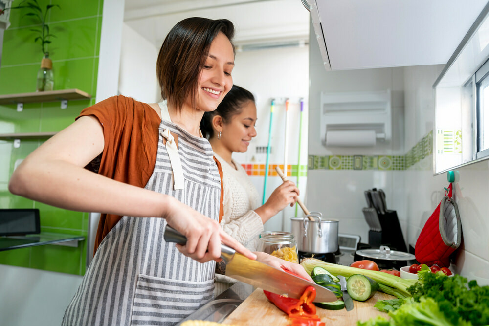 kitchen - two young women cooking, chopping and stirring food