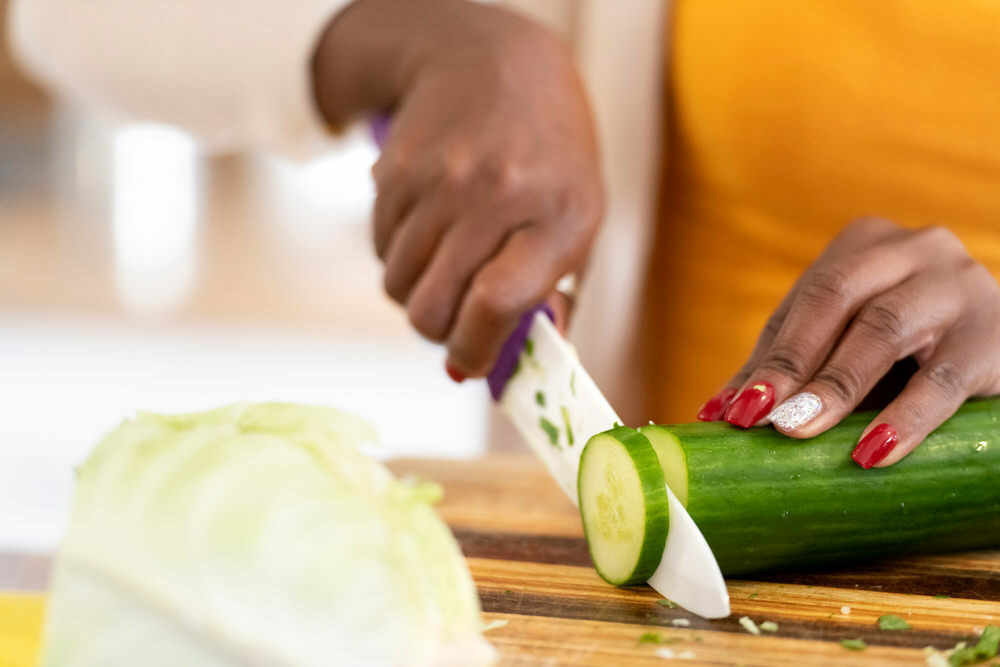 kitchen prep - brown hands with a chef knife cuttting a cucumber