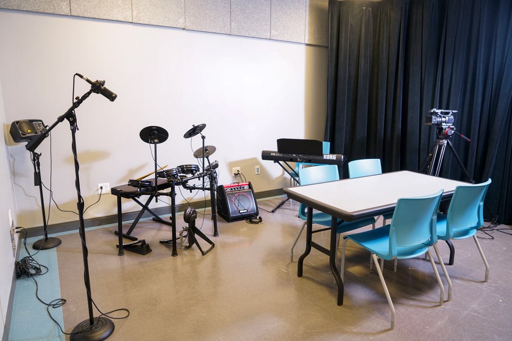 Teen Center video and production studio - wide view with table and chairs, musical equipment and recording gear