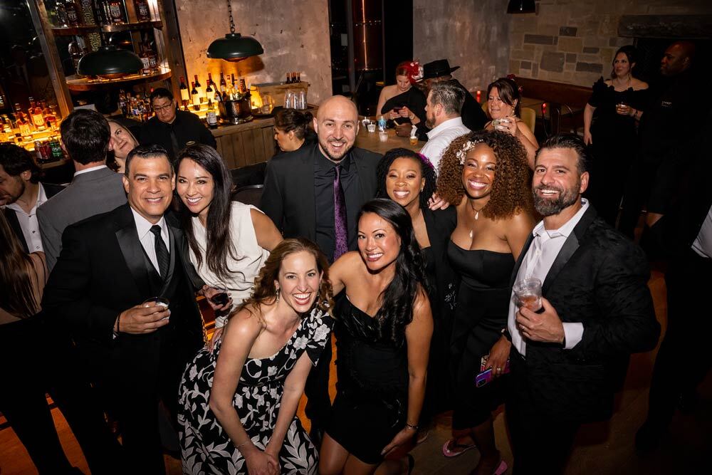 A group of people having fun at the 2022 Black & White Party, wearing black tie attire by a bar