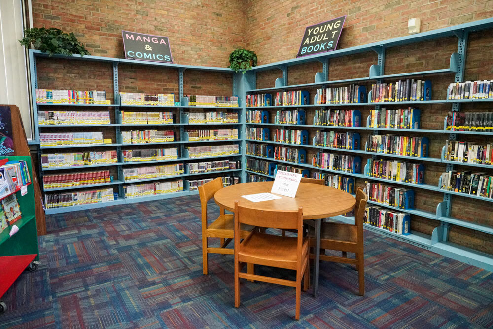 Brooklyn teens corner showing a teens-only table, bookshelves, and signs for young adult books, manga and comics