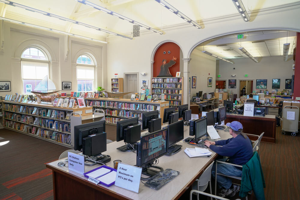 Canton interior view of a library room with bookshelves, windows, and a staff member working at a desk