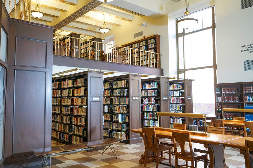 Central Library interior showing two levels with bookshelves, tables and chairs, and awindow