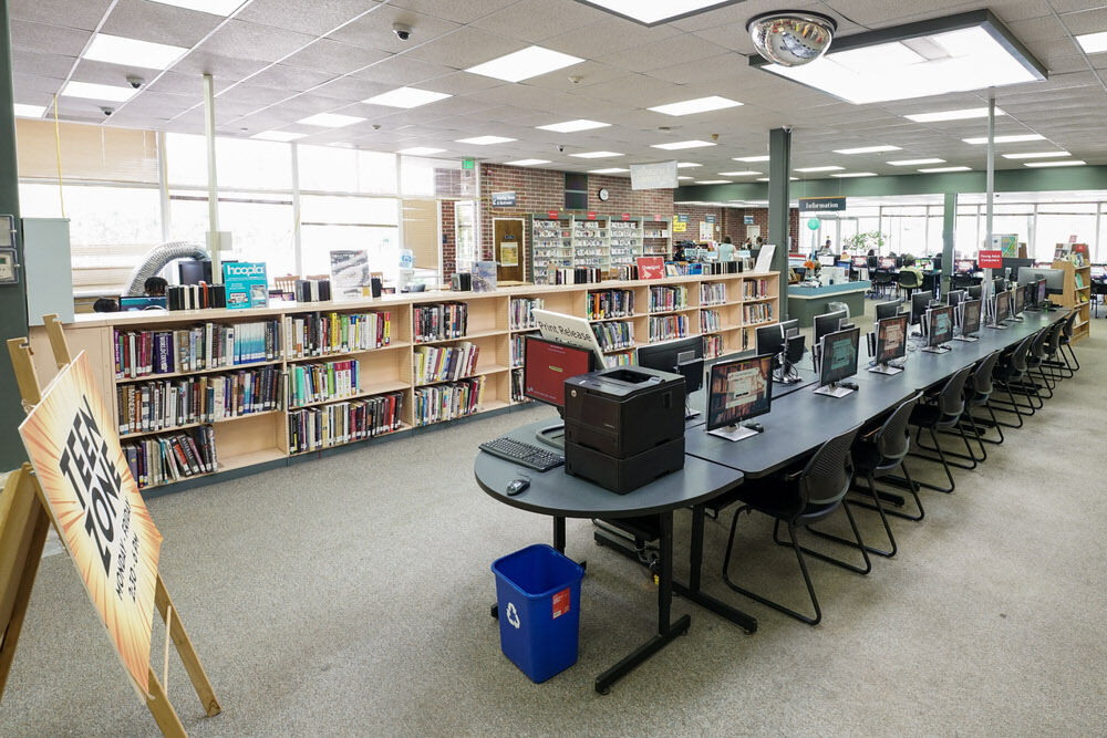 Hamilton Branch room with a table of public computers, Teen Zone sign, bookshelves, and windows