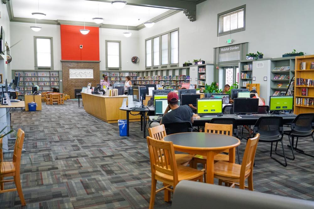 Patterson Park room with people using computers, bookshelves, and exit to the habitat garden