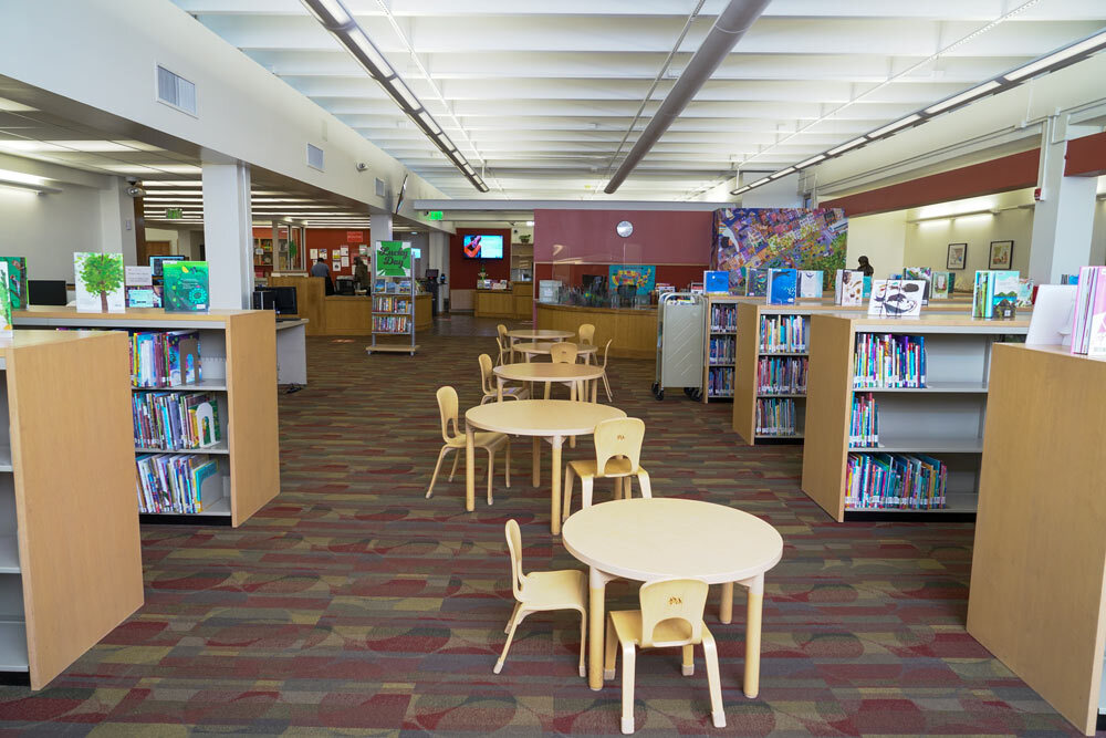 Reisterstown Road room with tables and chairs for kids, bookshelves, and a Lucky Day sign