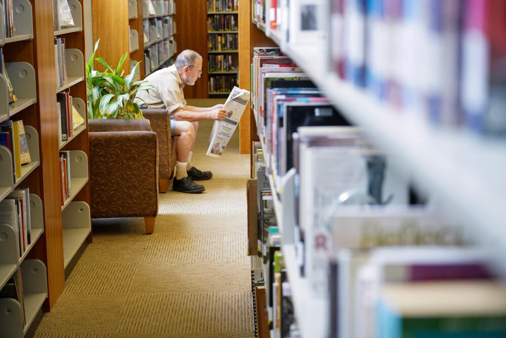 Roland Park  - a man reading in chair by plants among bookshelves