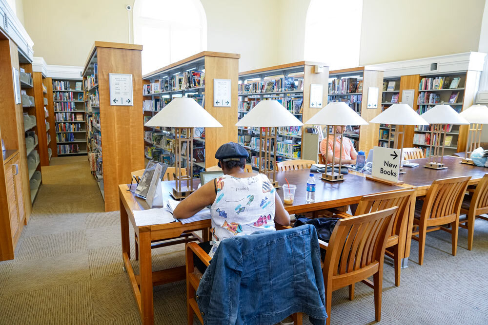 Roland Park table with lamps, people reading, bookshelves in the background