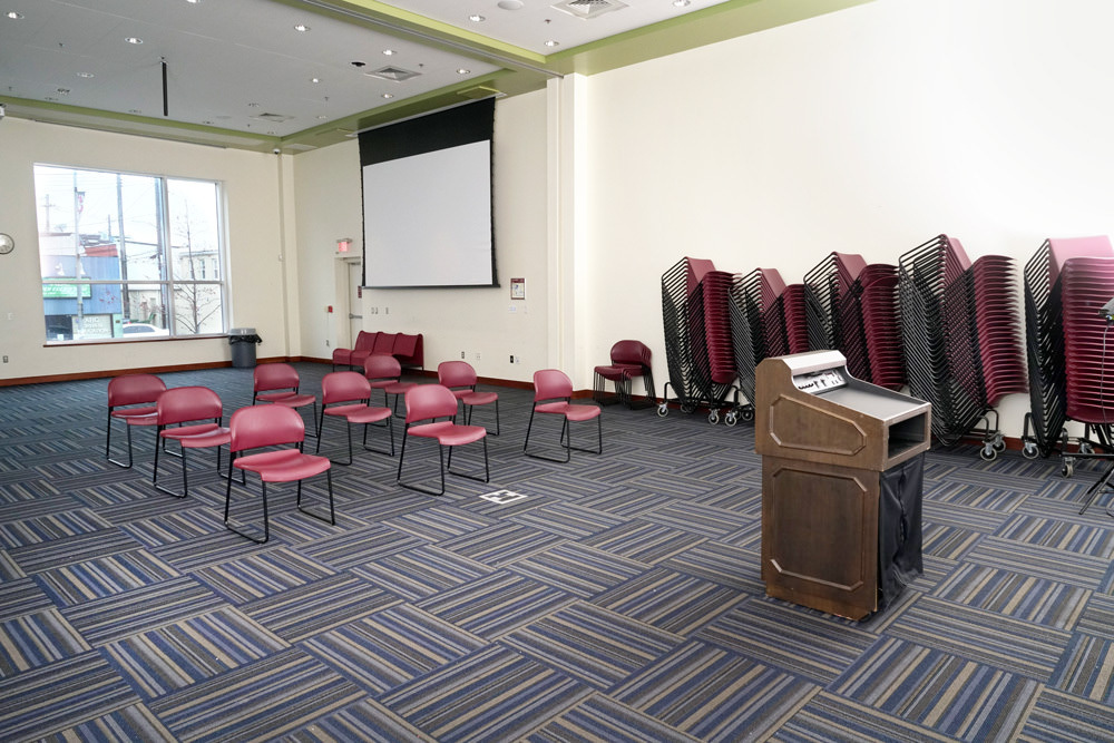 Southeast large meeting room - auditorium facing a corner with a view of the podium, chairs, screen, and windows