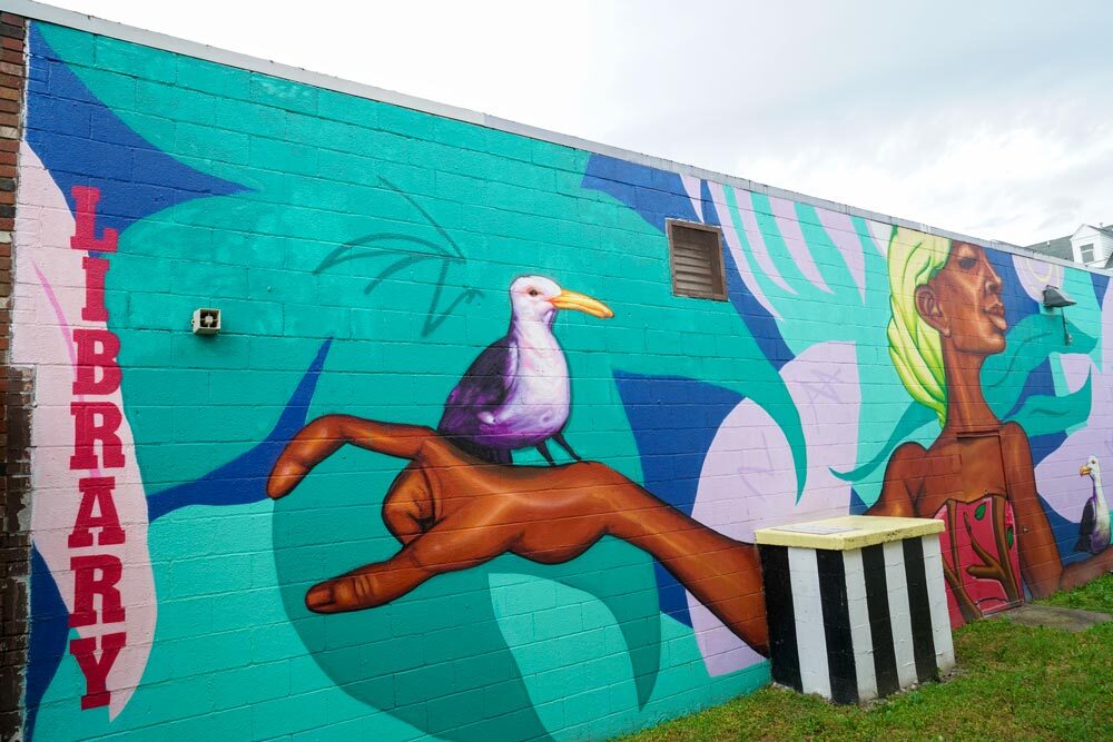 Washington Village outdoor mural with the word LIBRARY and a colorful scene with a woman and bird on a hand