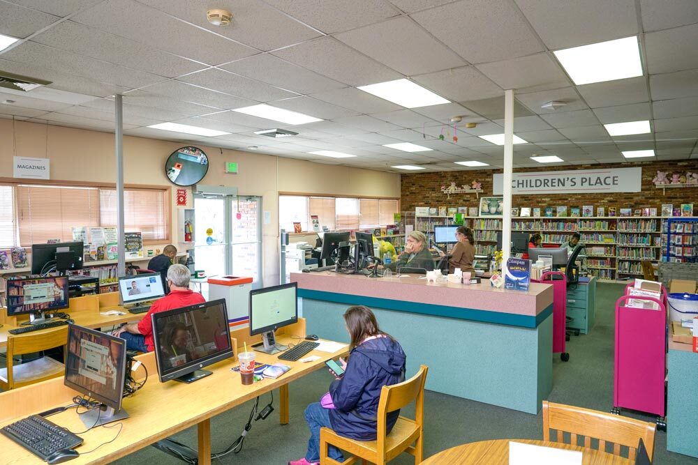 Washington Village - wide room view with people using computers, desks, and Children's Place in the background